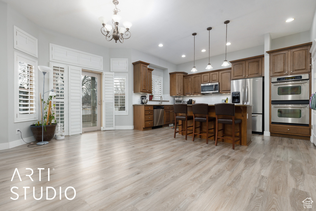 Kitchen with light wood-type flooring, hanging light fixtures, stainless steel appliances, a center island, and a kitchen bar