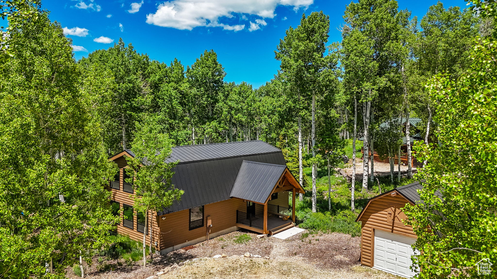 View of side of property featuring a porch, a garage, metal roof, dirt driveway, and an outdoor structure