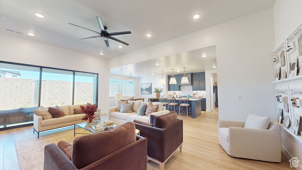 Living area featuring recessed lighting, baseboards, light wood-style floors, and ceiling fan with notable chandelier