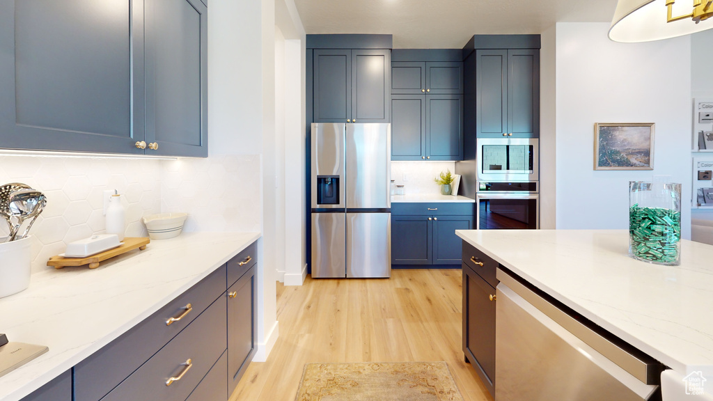 Kitchen featuring decorative backsplash, light stone countertops, light wood-type flooring, and appliances with stainless steel finishes