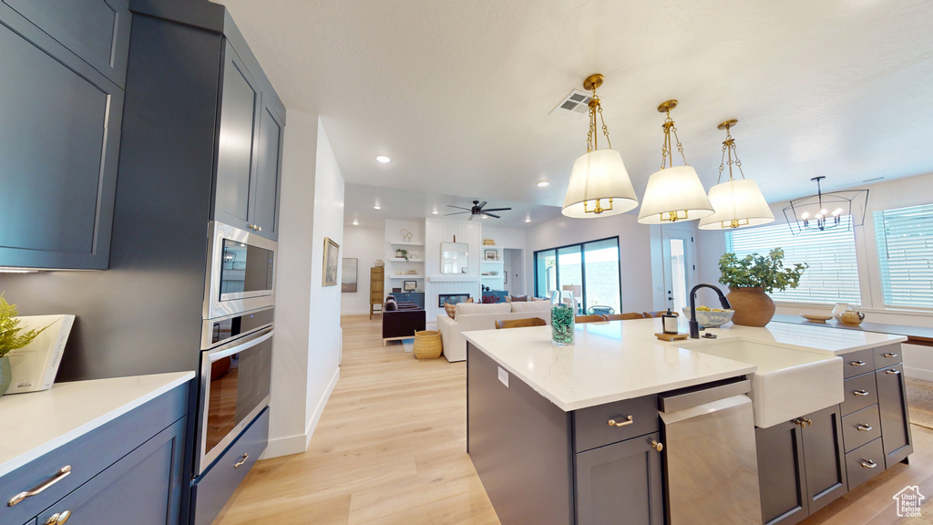 Kitchen with light wood-type flooring, visible vents, a sink, a glass covered fireplace, and stainless steel appliances
