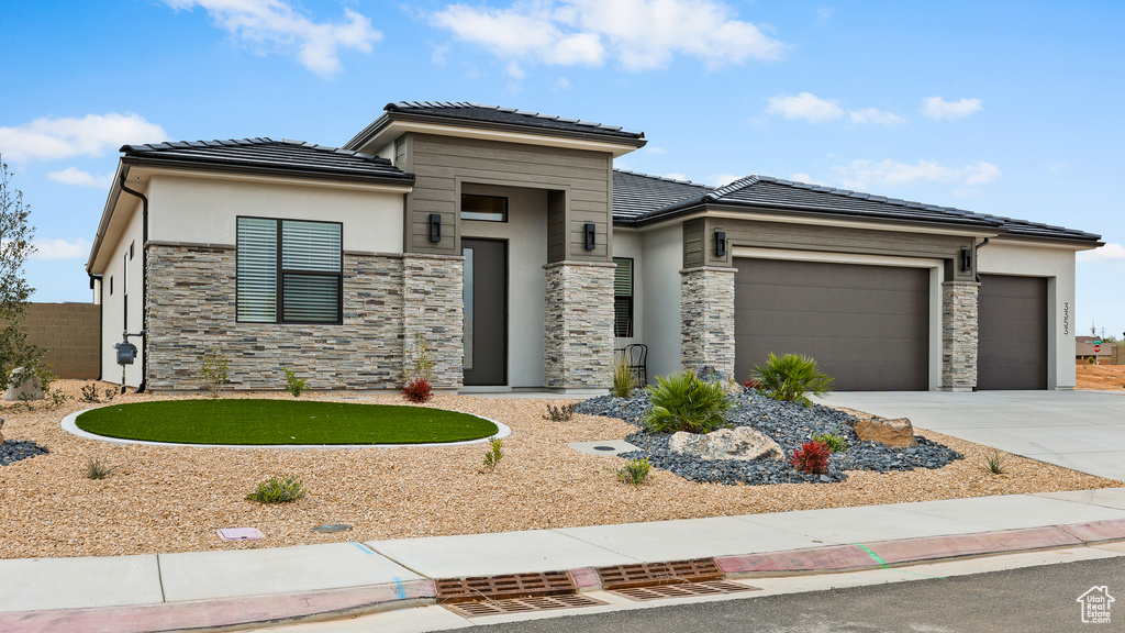 Prairie-style home featuring a tiled roof, an attached garage, stone siding, and driveway