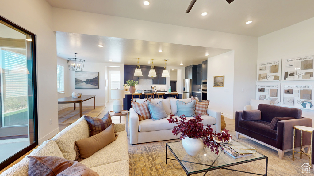 Living area featuring ceiling fan with notable chandelier, recessed lighting, baseboards, and light wood finished floors