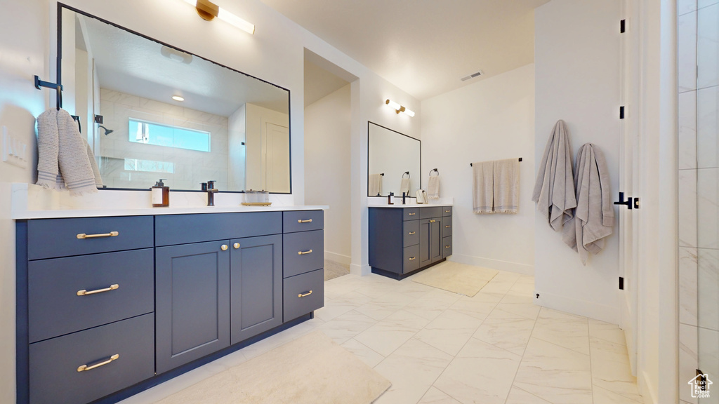 Bathroom featuring baseboards, two vanities, a tile shower, a sink, and marble finish floor