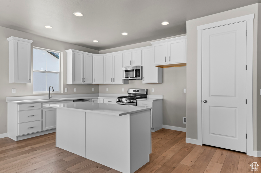 Kitchen featuring stainless steel appliances, a sink, light wood-style flooring, white cabinetry, and baseboards