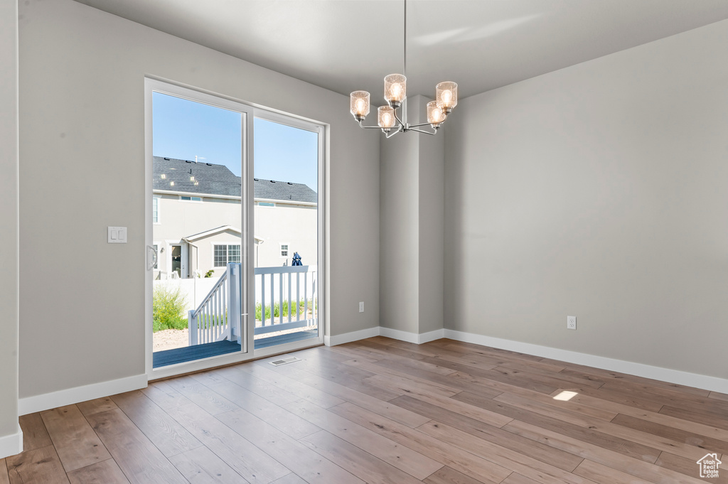Empty room featuring a chandelier, hardwood / wood-style floors, and baseboards