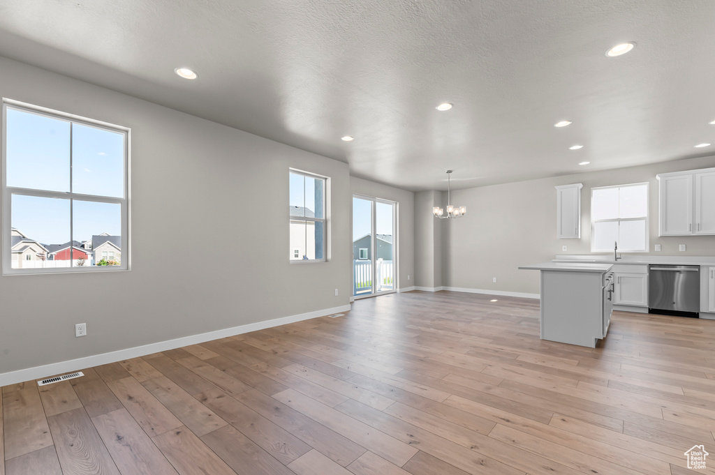 Unfurnished living room featuring a chandelier, baseboards, recessed lighting, light wood finished floors, and a sink