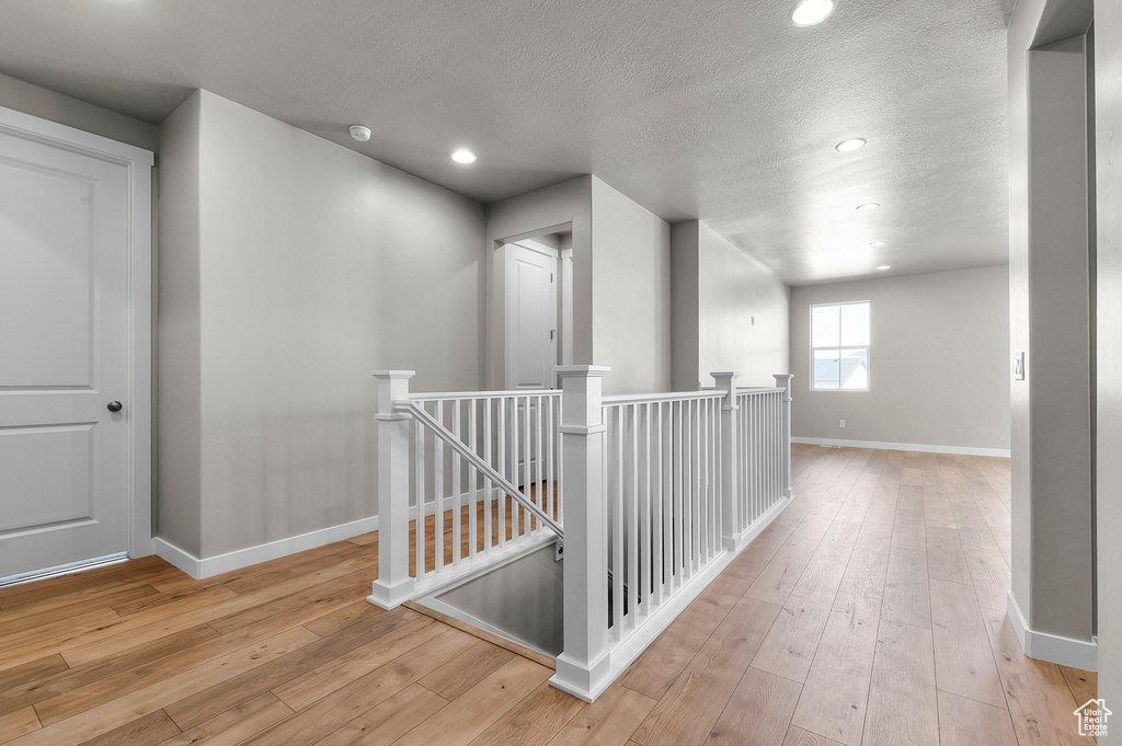 Hall with an upstairs landing, baseboards, hardwood / wood-style floors, a textured ceiling, and recessed lighting