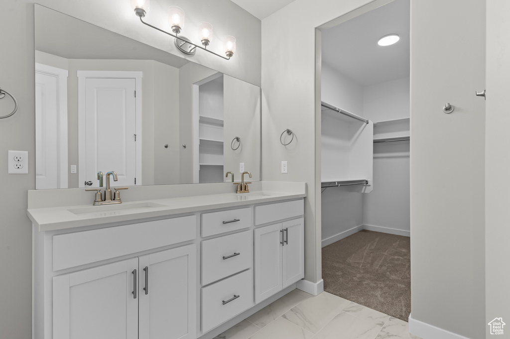 Bathroom featuring double vanity, baseboards, a walk in closet, and marble finish flooring