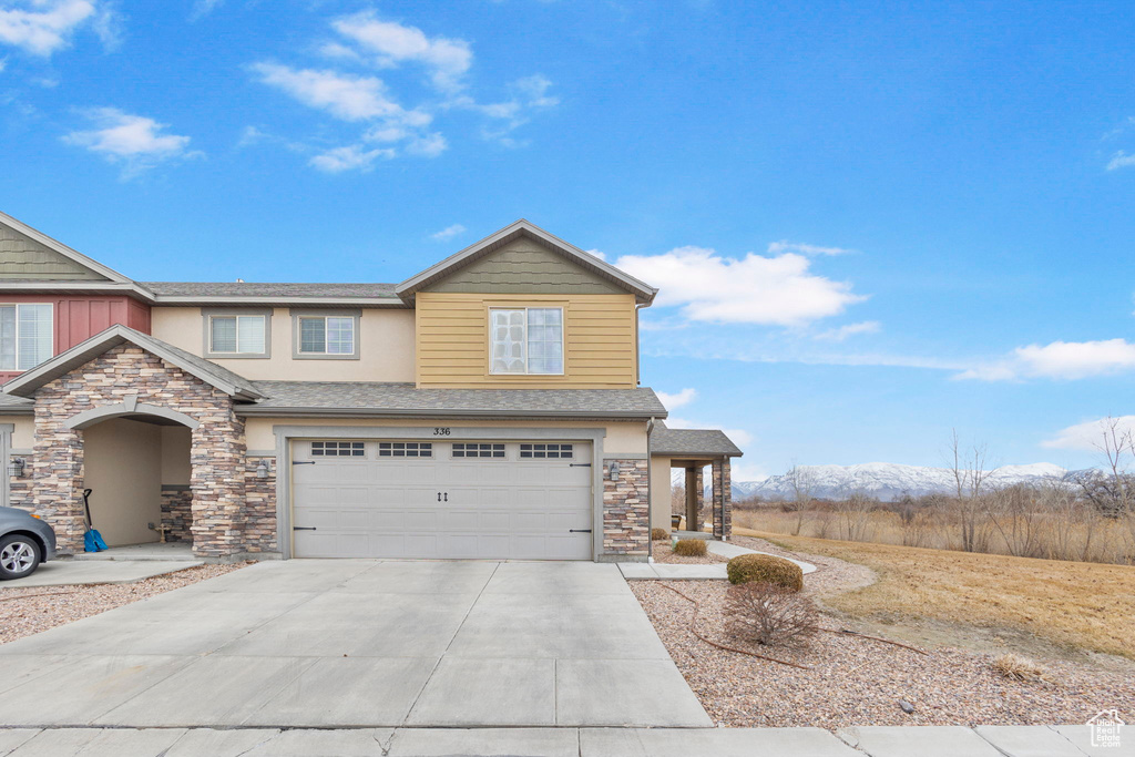 View of front of house with concrete driveway, stone siding, an attached garage, a mountain view, and stucco siding