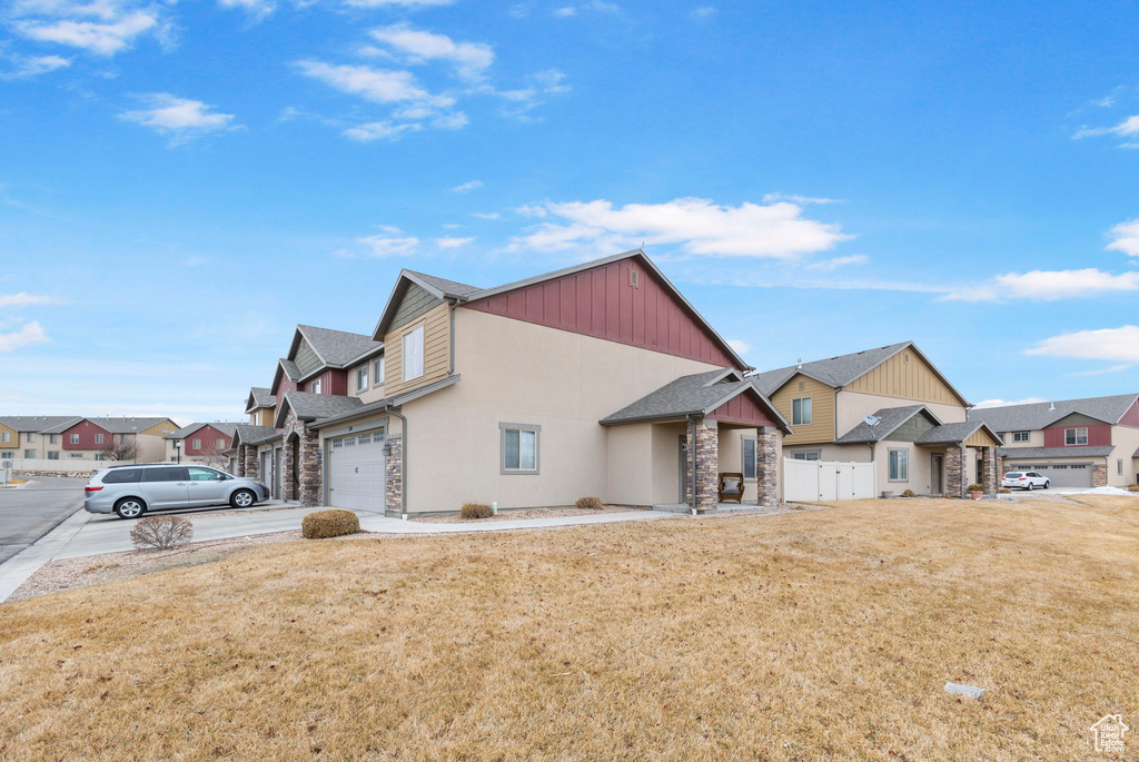 View of front of property with concrete driveway, a front lawn, stone siding, and a residential view