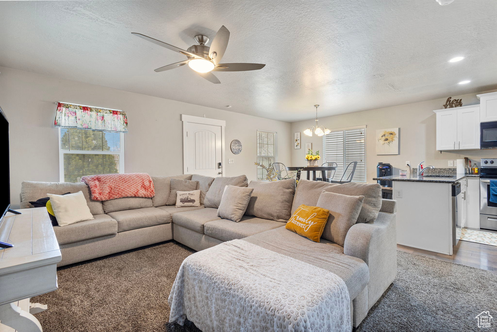 Living room with a textured ceiling, ceiling fan with notable chandelier, dark wood finished floors, and recessed lighting