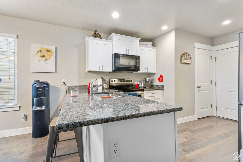 Kitchen with black microwave, a peninsula, a sink, white cabinetry, and stainless steel range with electric cooktop