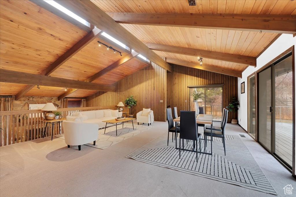 Dining space with wood walls, light colored carpet, lofted ceiling with beams, and wood ceiling