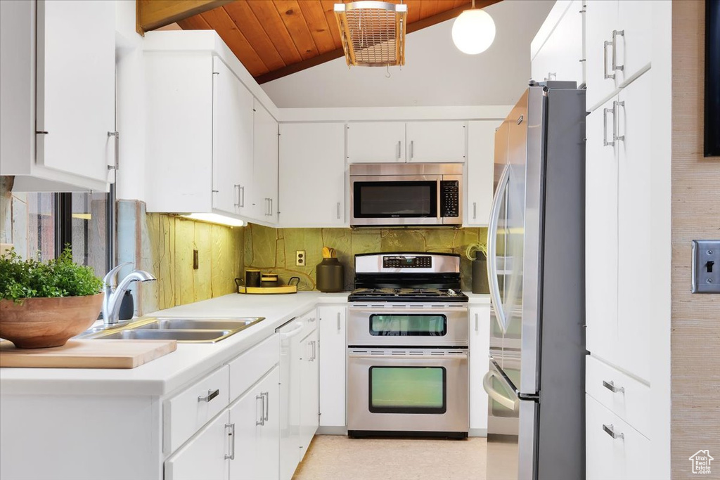 Kitchen featuring stainless steel appliances, sink, vaulted ceiling, white cabinets, and decorative backsplash