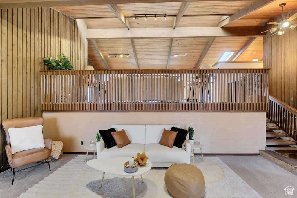 Living room featuring wood ceiling, lofted ceiling with beams, ceiling fan, wooden walls, and rail lighting