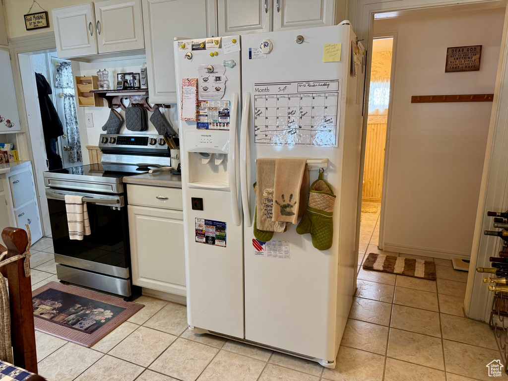 Kitchen with light tile patterned floors, white fridge with ice dispenser, white cabinets, and stainless steel electric stove