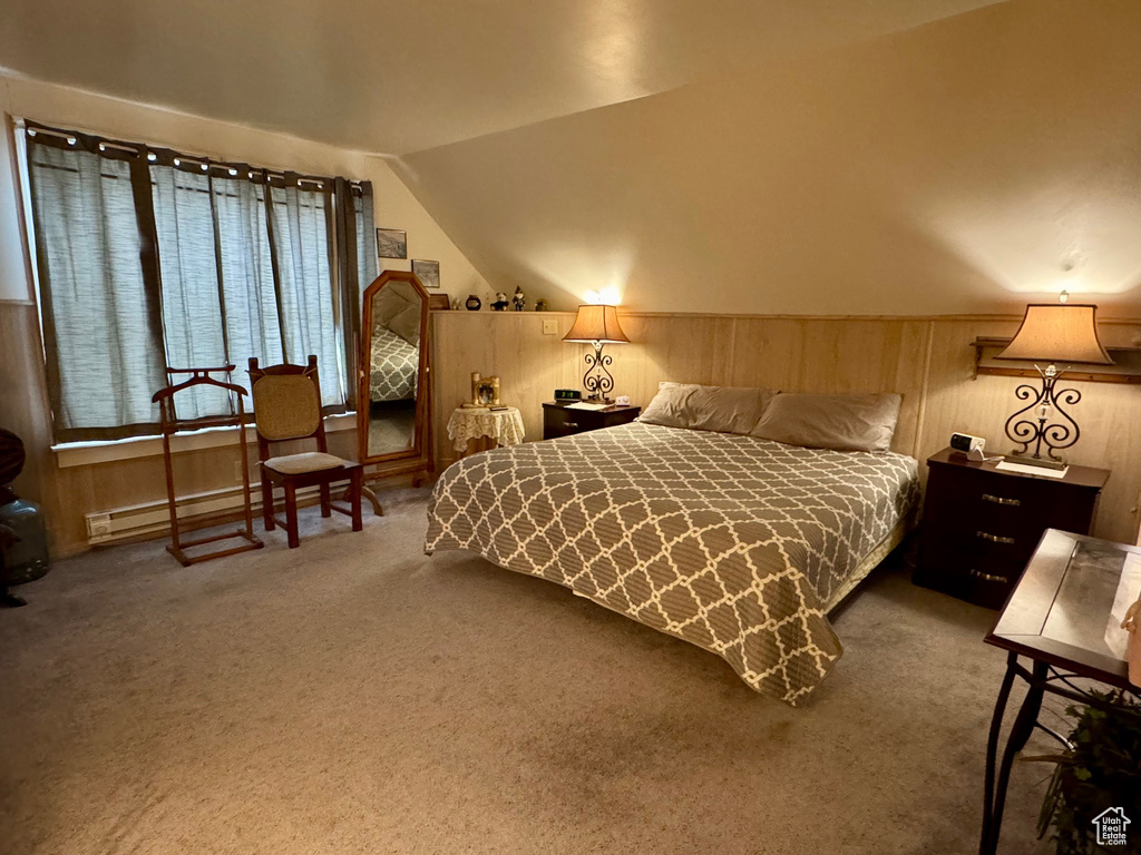 Carpeted bedroom with lofted ceiling, a wainscoted wall, wooden walls, and baseboard heating