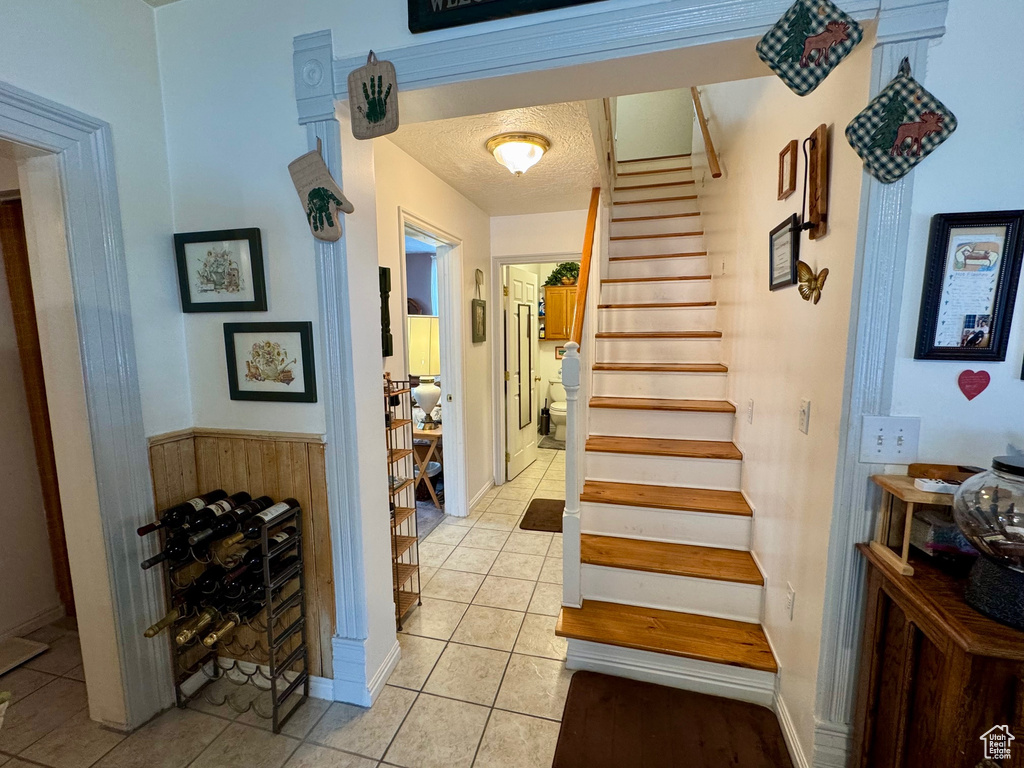 Stairway featuring tile patterned floors, wood walls, a textured ceiling, and wainscoting