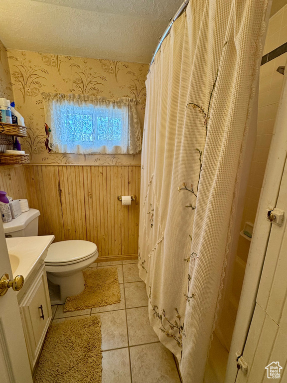 Bathroom with a textured ceiling, wainscoting, vanity, and wallpapered walls