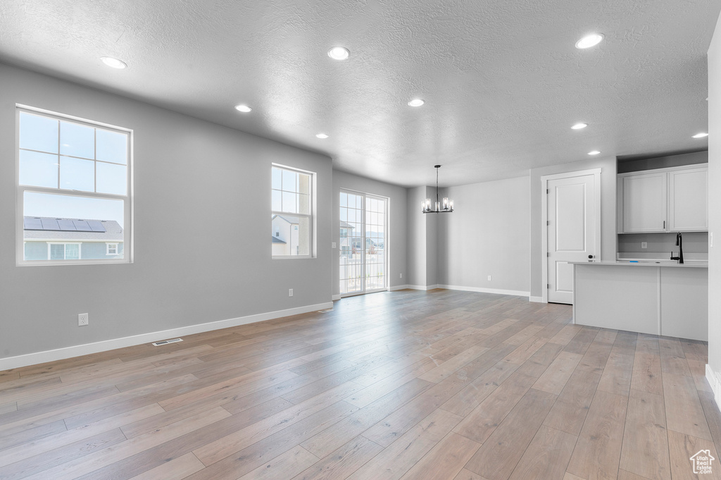 Unfurnished living room with a chandelier, a textured ceiling, recessed lighting, light wood-style flooring, and baseboards