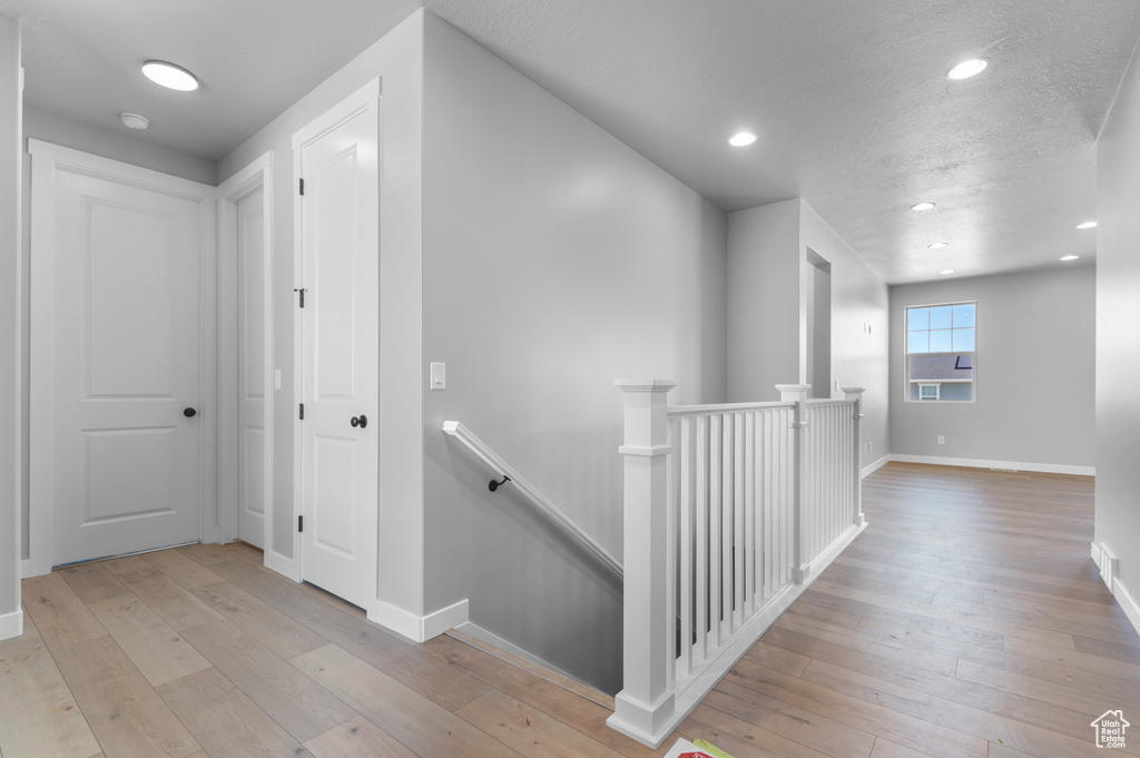 Hallway with an upstairs landing, light wood-type flooring, baseboards, and recessed lighting