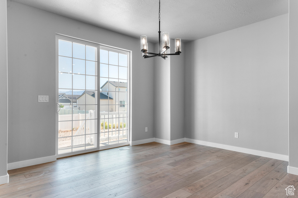 Unfurnished room featuring a chandelier, plenty of natural light, and light wood-style flooring