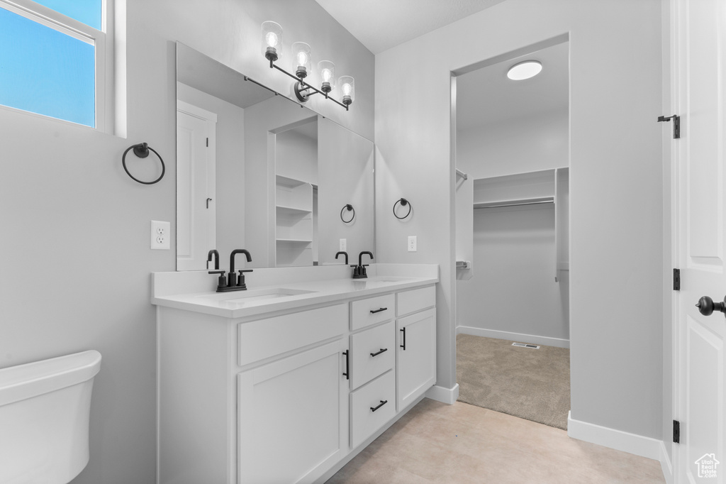 Full bath with double vanity, toilet, a walk in closet, and baseboards