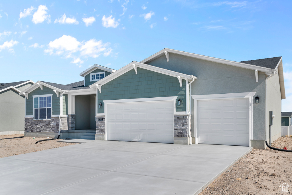 View of front of property with an attached garage, driveway, and stone siding