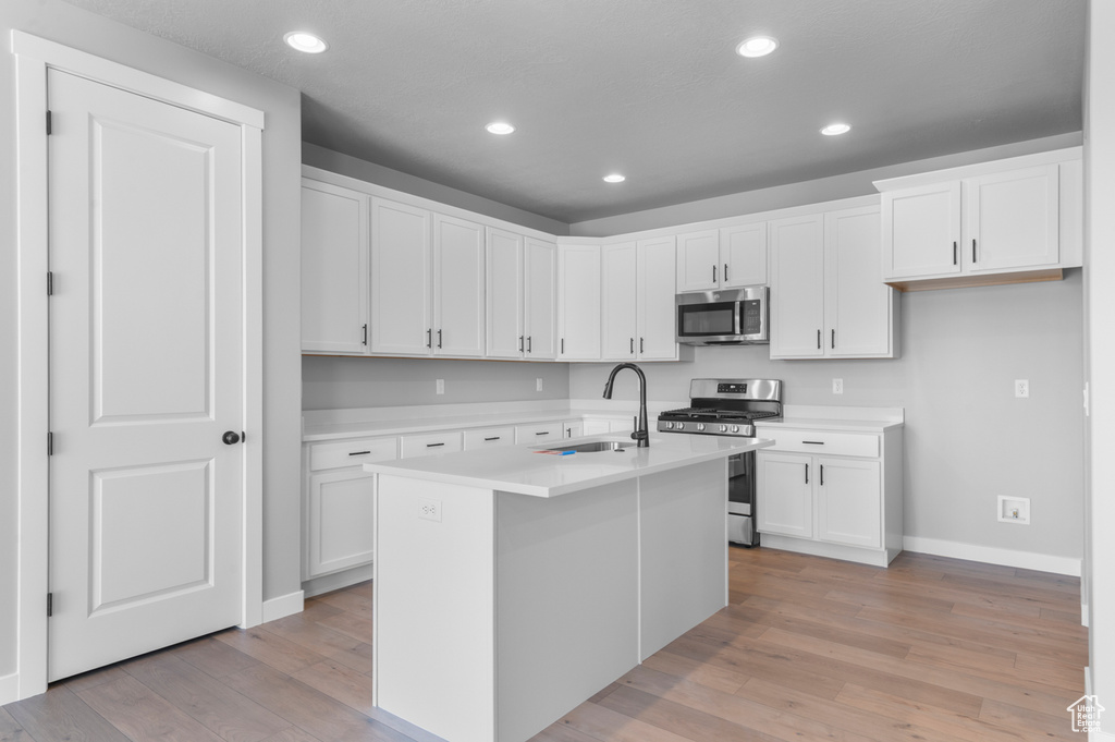 Kitchen with appliances with stainless steel finishes, a sink, baseboards, light wood-style floors, and white cabinets