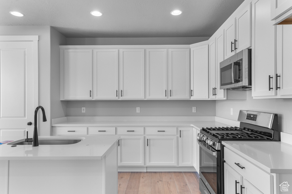 Kitchen with appliances with stainless steel finishes, a sink, light countertops, white cabinetry, and recessed lighting