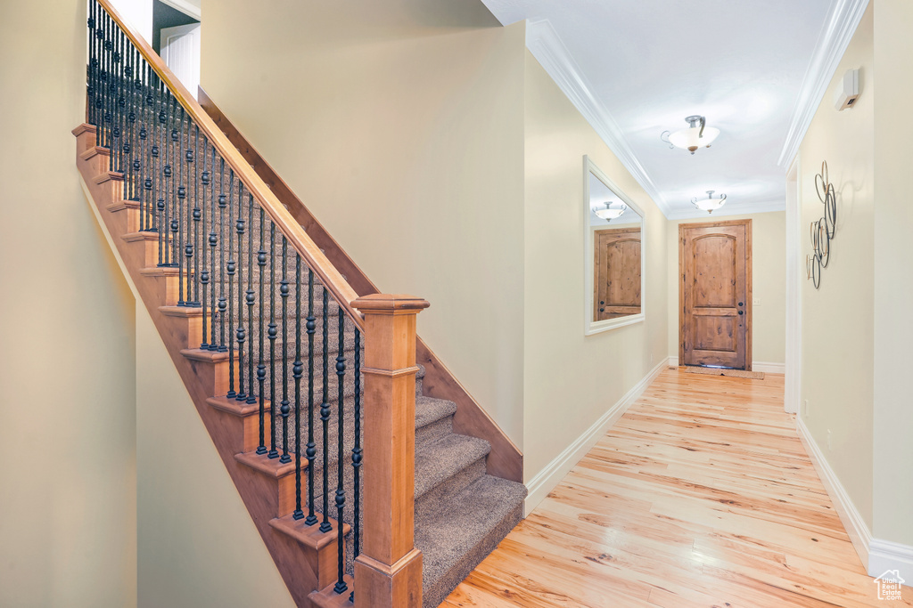Hallway with crown molding, stairway, baseboards, and light wood-style floors