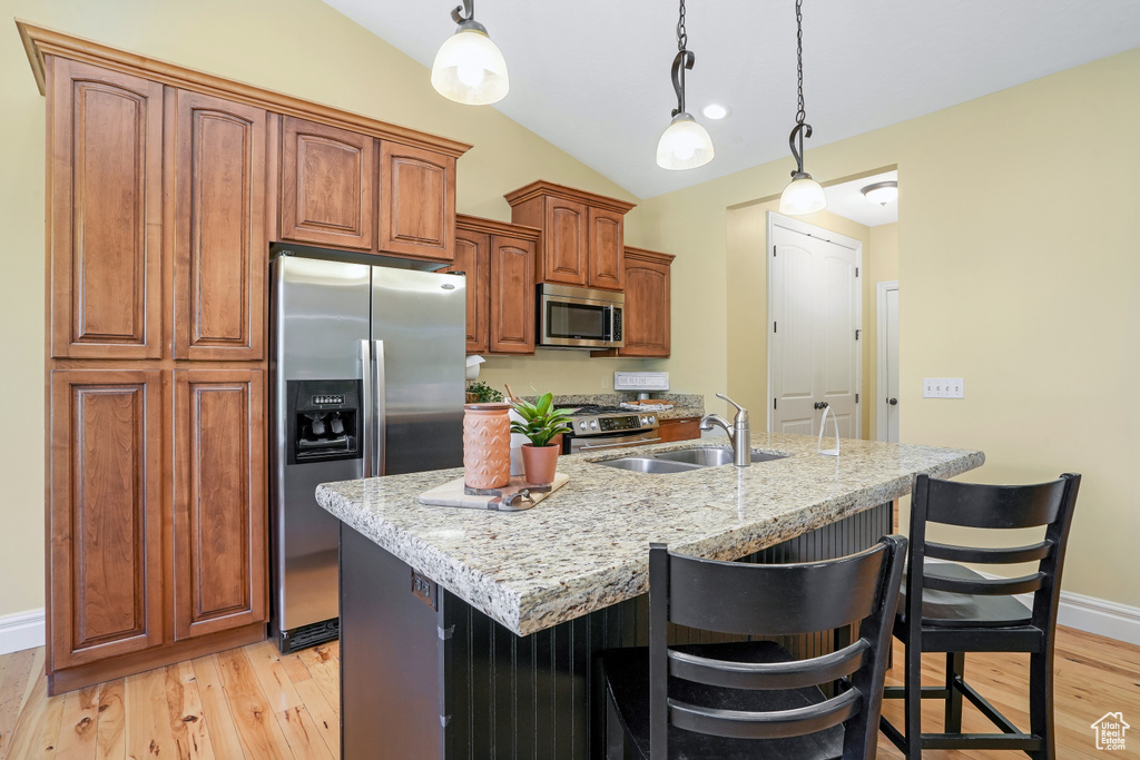 Kitchen featuring stainless steel appliances, light stone counters, brown cabinetry, and a kitchen island with sink