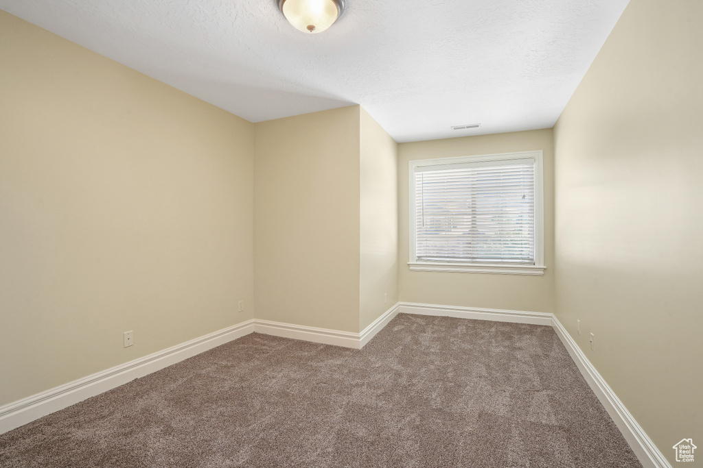 Carpeted spare room with a textured ceiling, visible vents, and baseboards