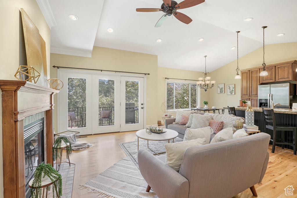 Living area featuring light wood-type flooring, a tile fireplace, vaulted ceiling, and ceiling fan with notable chandelier