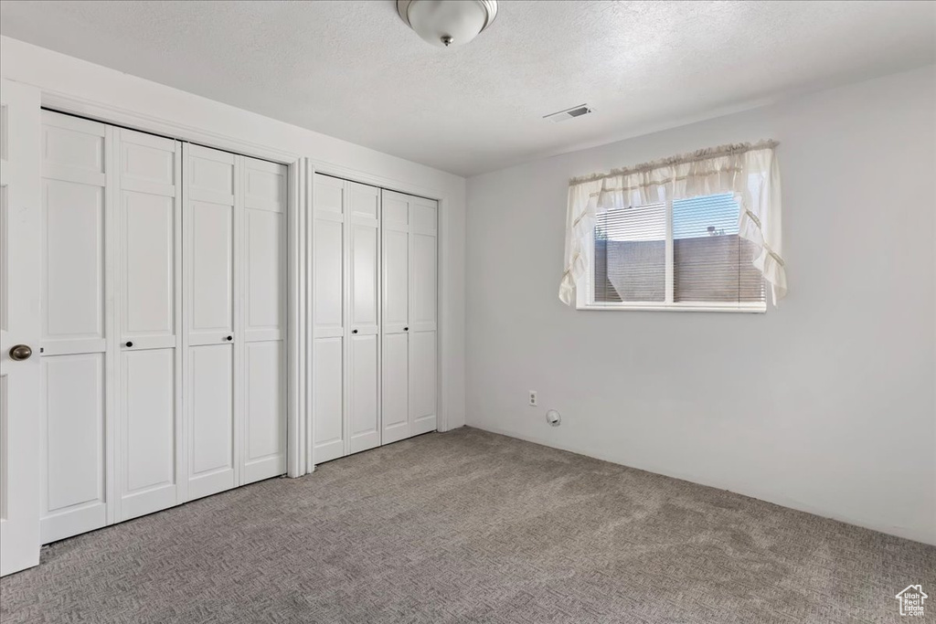 Unfurnished bedroom with carpet, a textured ceiling, visible vents, and multiple closets