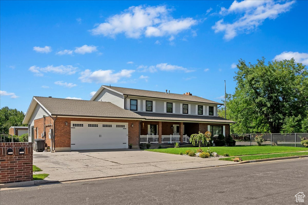 View of front of property with a garage, driveway, brick siding, fence, and a front yard