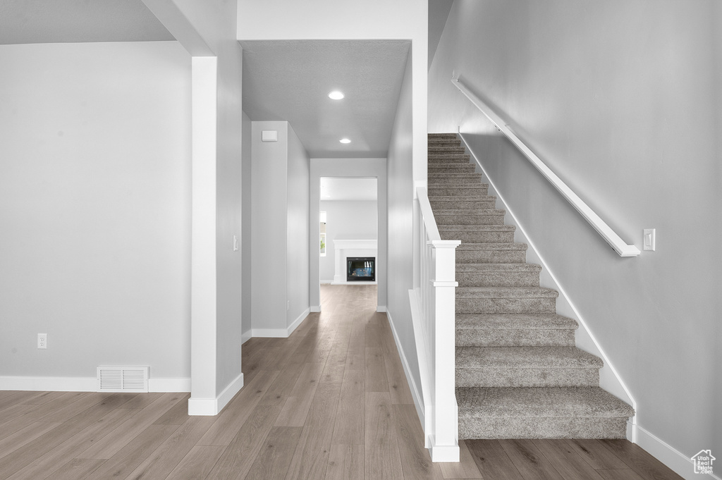 Stairway with wood finished floors, recessed lighting, baseboards, and a glass covered fireplace
