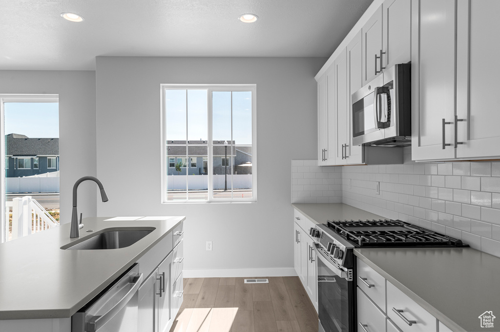Kitchen featuring appliances with stainless steel finishes, a sink, light wood finished floors, recessed lighting, and backsplash