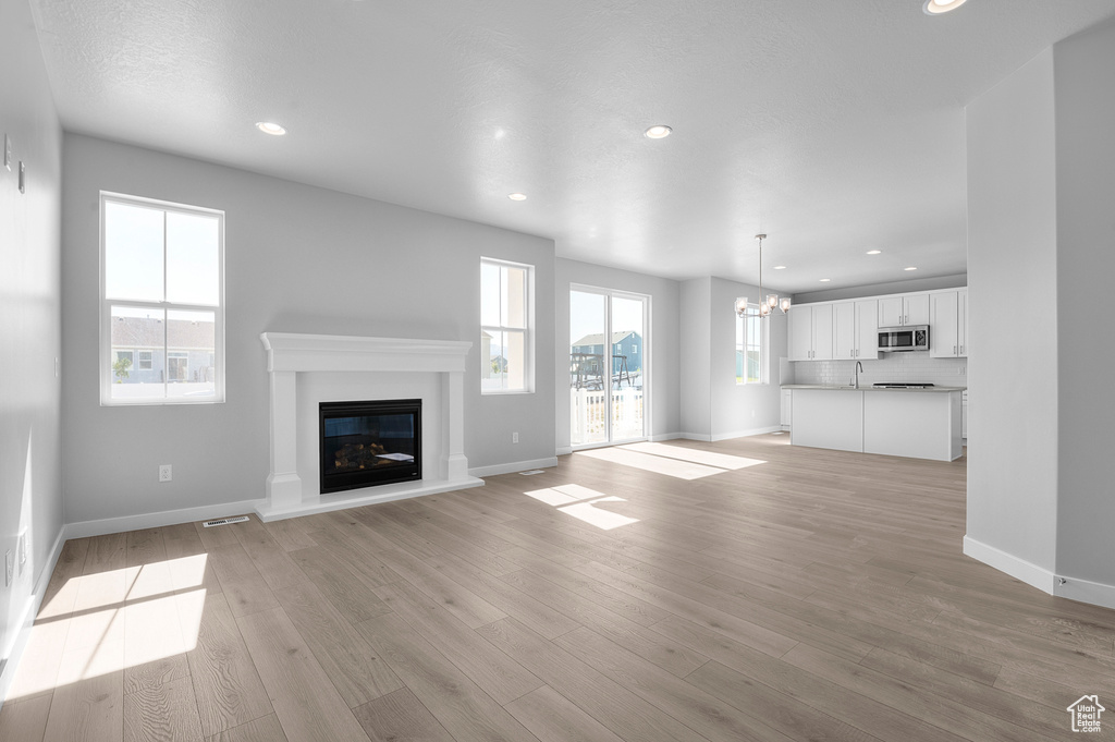 Unfurnished living room with a glass covered fireplace, baseboards, recessed lighting, light wood finished floors, and a chandelier