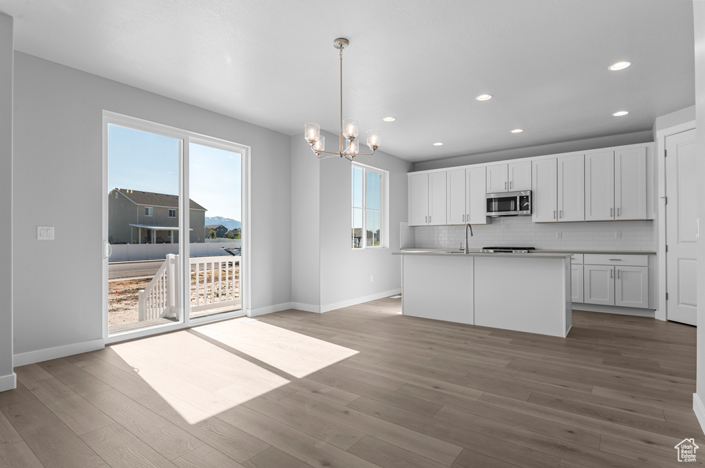 Kitchen with stainless steel microwave, baseboards, a chandelier, white cabinetry, and recessed lighting