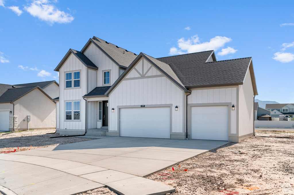 Modern farmhouse featuring a shingled roof, a garage, driveway, and board and batten siding