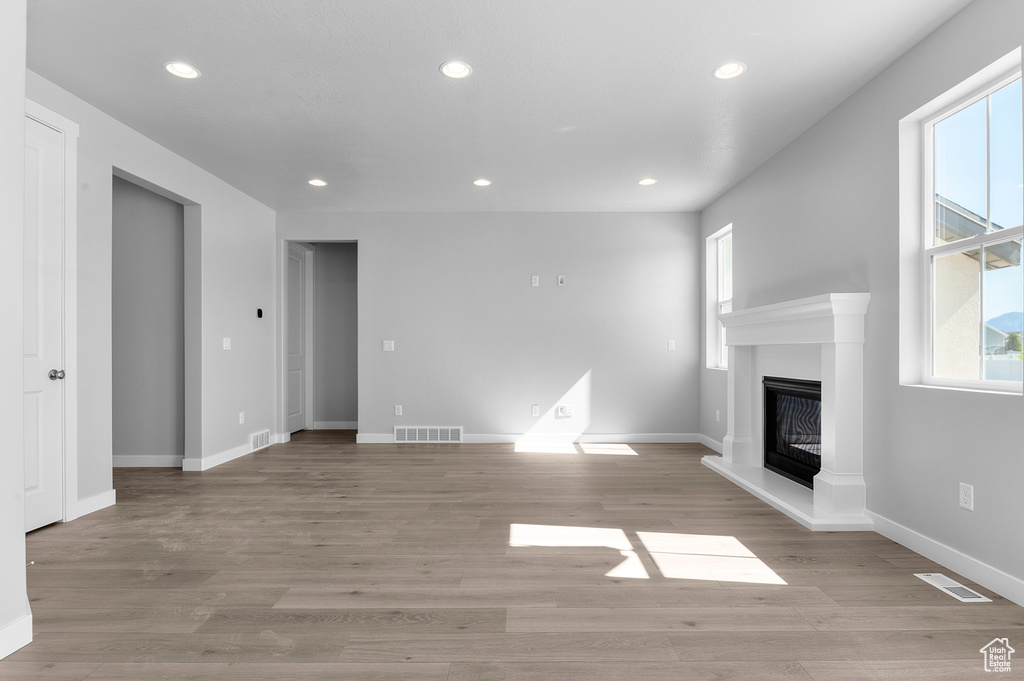 Unfurnished living room with recessed lighting, a glass covered fireplace, baseboards, and light wood finished floors