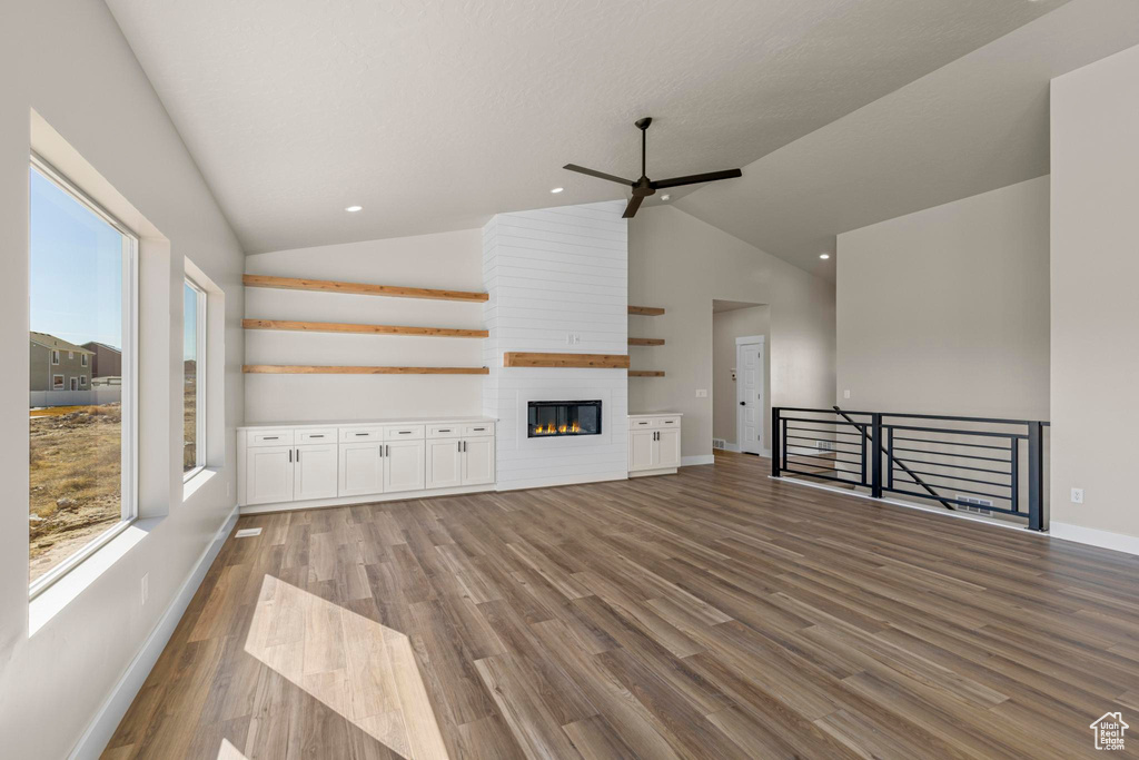 Unfurnished living room featuring lofted ceiling, plenty of natural light, a fireplace, and wood finished floors