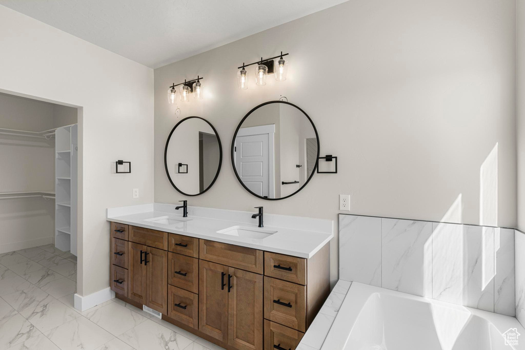 Full bath featuring double vanity, marble finish floor, baseboards, and a sink