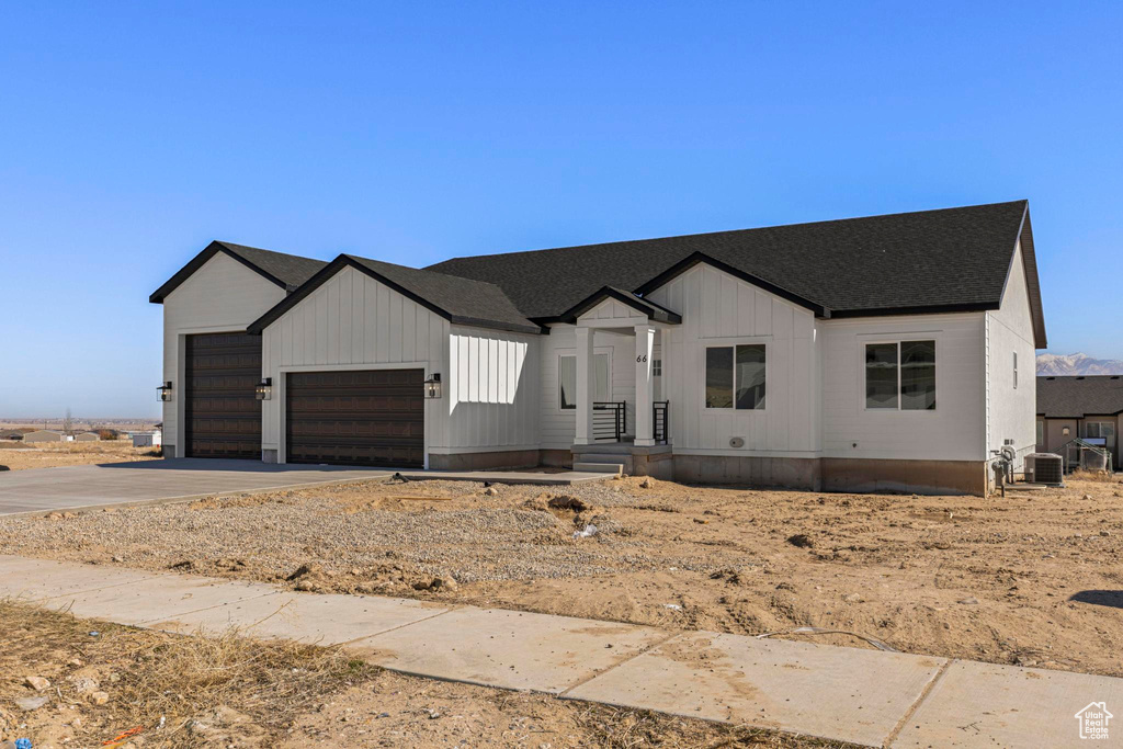 Modern farmhouse featuring a garage, driveway, central AC unit, and a shingled roof