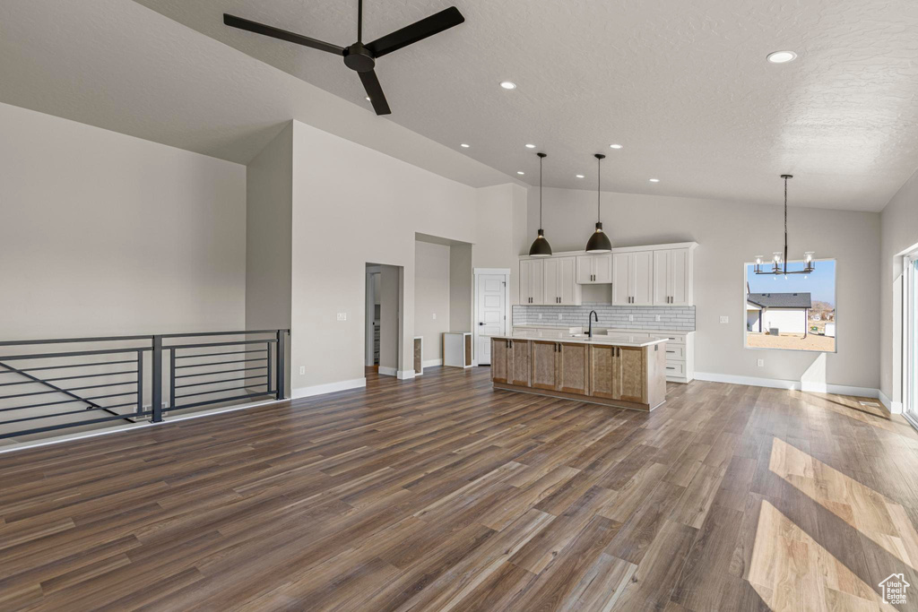 Kitchen featuring a center island with sink, white cabinets, open floor plan, dark wood-style flooring, and a sink