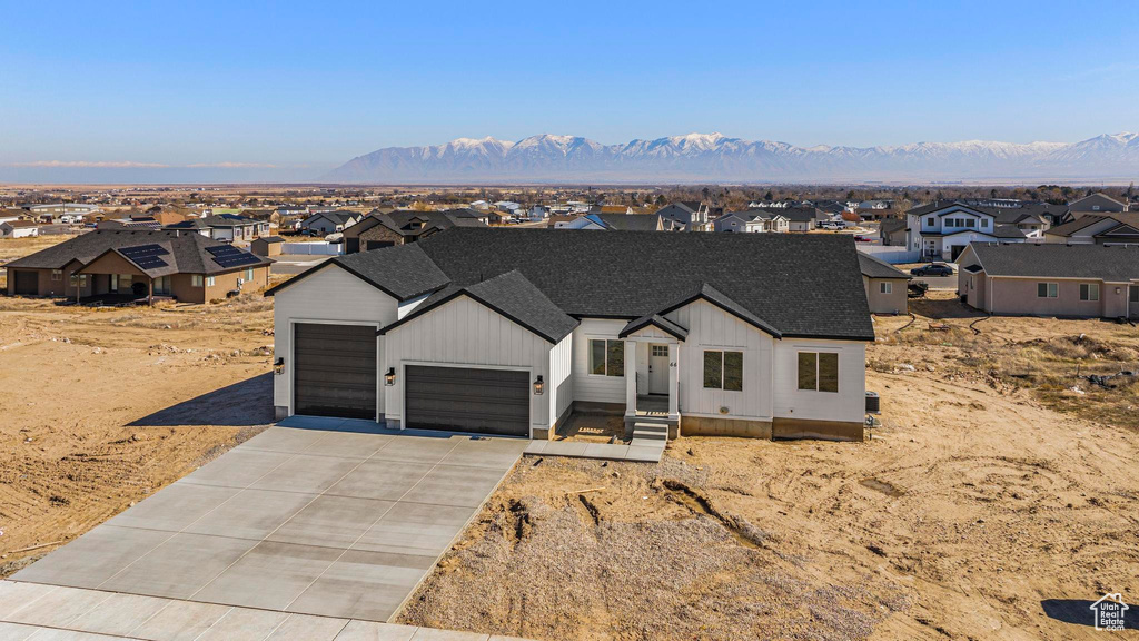 Modern farmhouse featuring concrete driveway, a residential view, roof with shingles, an attached garage, and a mountain view