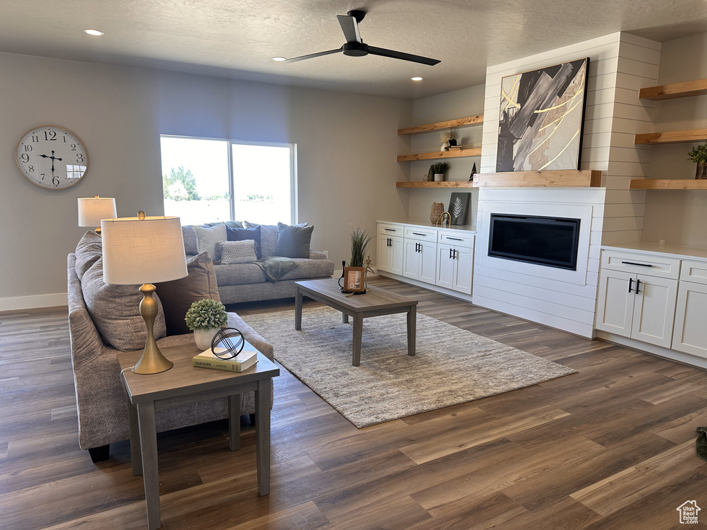 Living room with ceiling fan, recessed lighting, dark wood-type flooring, baseboards, and a large fireplace