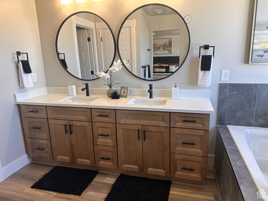 Bathroom with double vanity, tiled tub, and wood finished floors